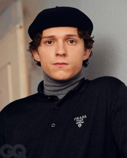 Close-up studio shot of an adult male wearing a black beret and polo shirt with a gray turtleneck underneath, looking at the camera.