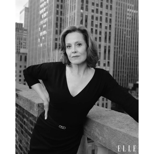 Black and white portrait of Sigourney Weaver in a black dress, set against the New York City skyline on a rooftop, with the ELLE logo.