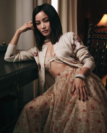 Woman with dark hair seated indoors wearing a floral cardigan and matching skirt photographed by Sharif Hamza