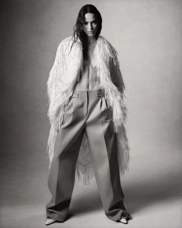 Fashion shot of a woman in wide-leg pants and a fringed coat, posing in a studio with medium shot and monochromatic palette.