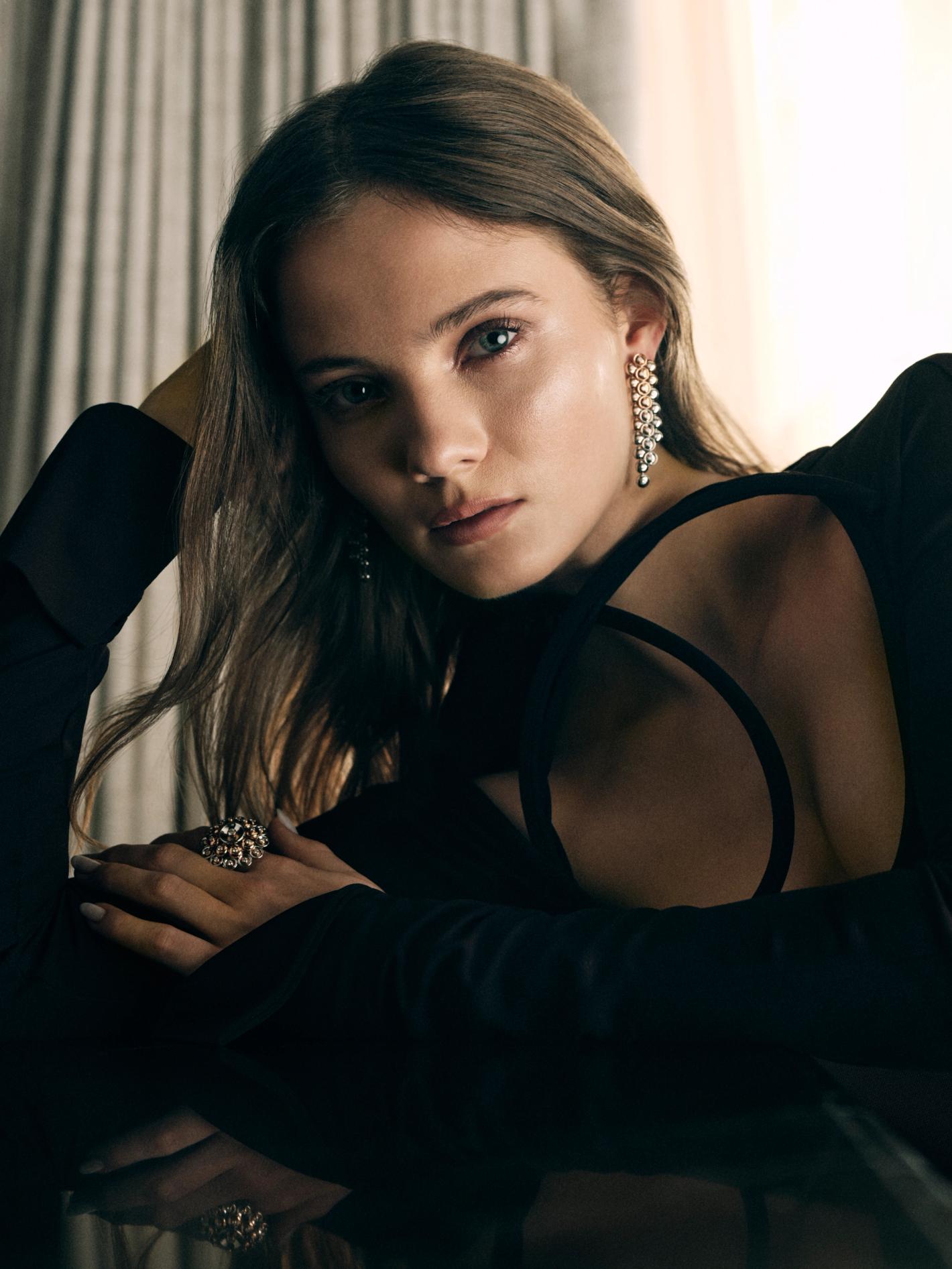 Close-up portrait of a woman in a black dress wearing pearl drop earrings and a statement ring, photographed by Sharif Hamza.