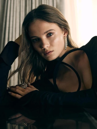 Close-up portrait of a woman in a black dress wearing pearl drop earrings and a statement ring, photographed by Sharif Hamza.
