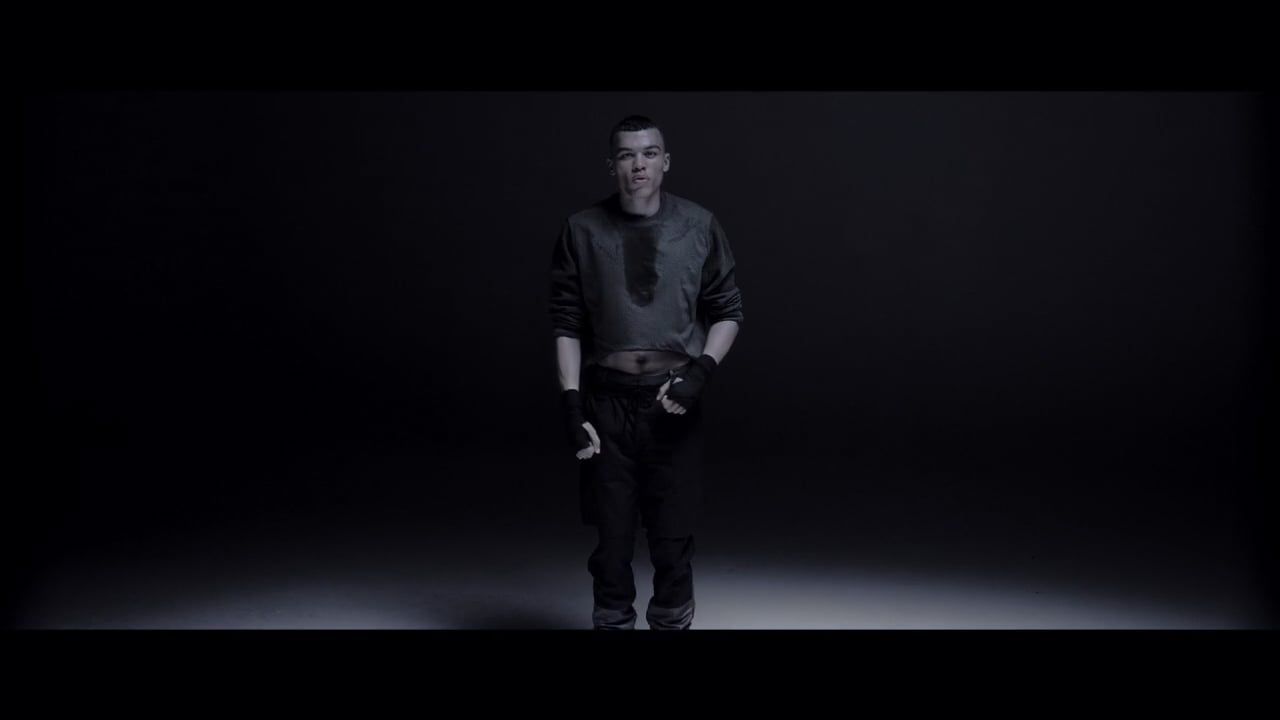 Adult male performs fitness activity in a dark, photo studio setting with visible perspiration and physical exertion in black activewear.