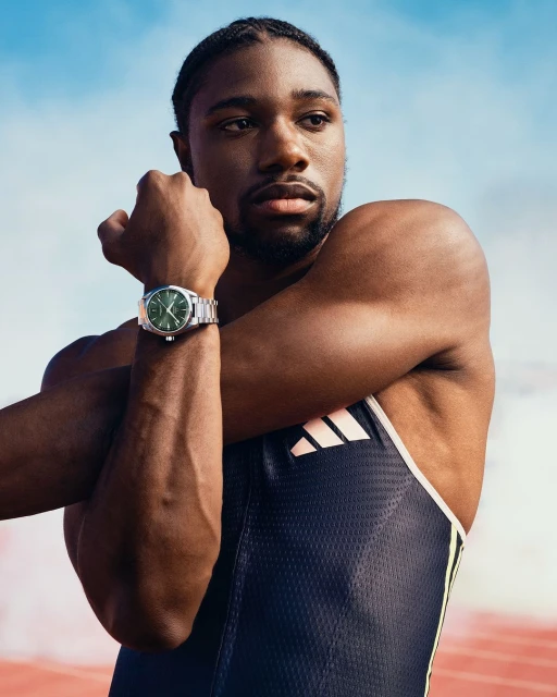 African American male athlete in running suit stretching arms outdoors wearing a stainless steel watch against a partly cloudy sky.