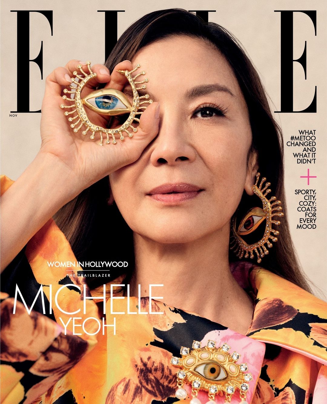 Michelle Yeoh on Elle magazine cover wearing a floral outfit and holding jewelry resembling an eye near her face.