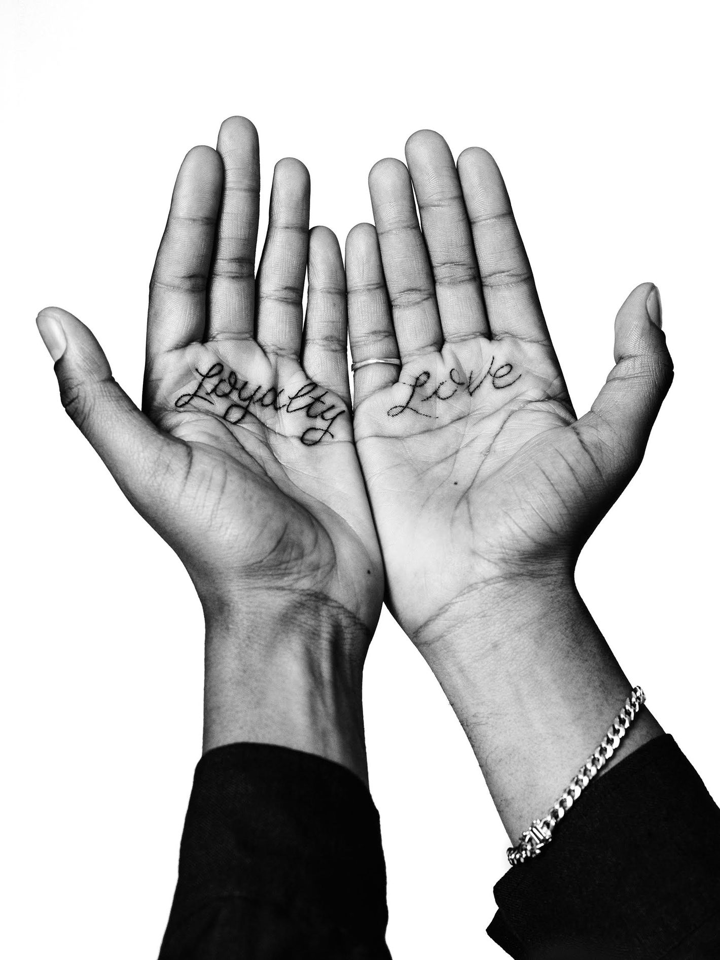Monochrome close-up of two open hands with 'loyalty' tattooed on the left palm and 'love' on the right, against a stark white background.