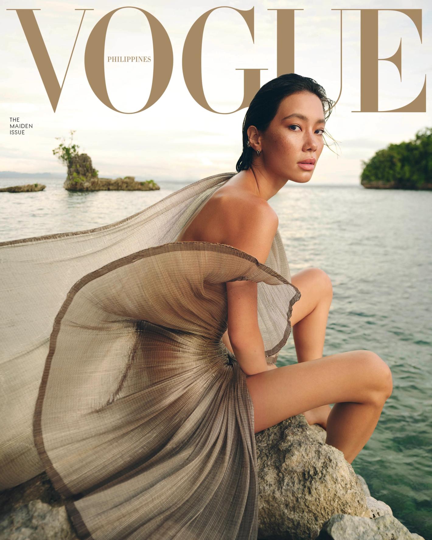 Vogue Philippines cover featuring an Asian female model in flowing beige dress sitting on a rock by the ocean with island backdrop.