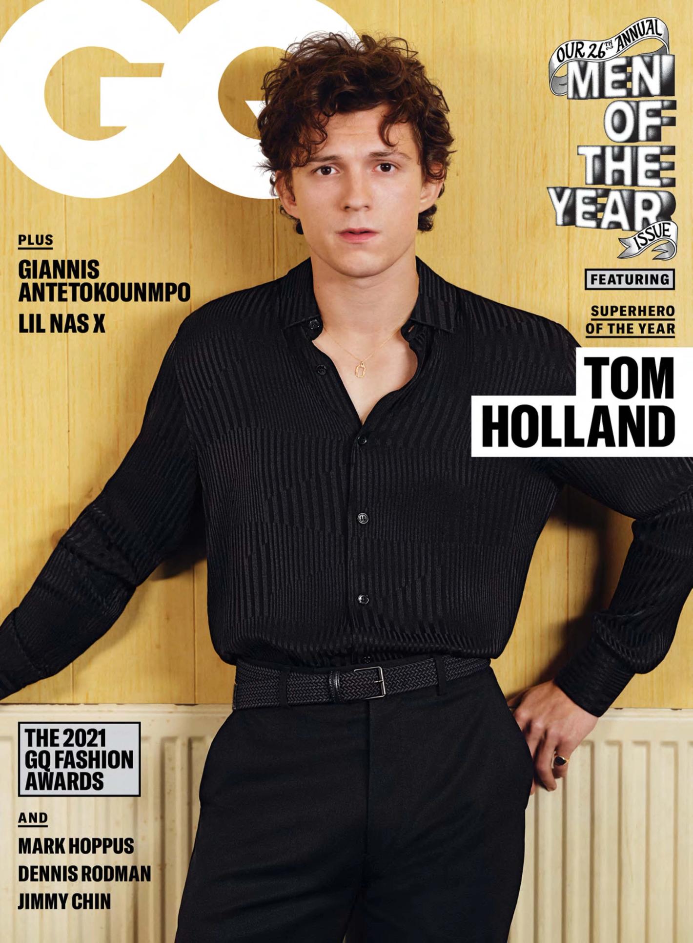 GQ magazine cover featuring Tom Holland in a pleated black shirt and matching pants, leaning against a light wood-paneled wall.