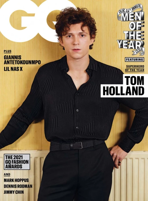GQ magazine cover featuring Tom Holland in a pleated black shirt and matching pants, leaning against a light wood-paneled wall.