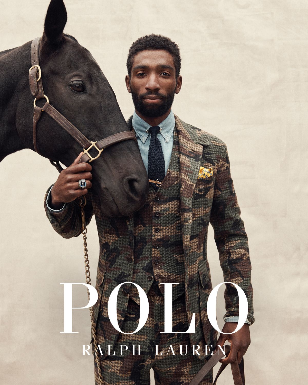 Black man in a camouflage suit stands with a black horse, both elegantly posed against a neutral backdrop for a Ralph Lauren ad.