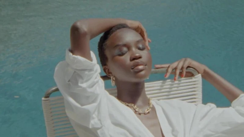 Woman in white shirt and gold chain necklace relaxing on a poolside lounger by water