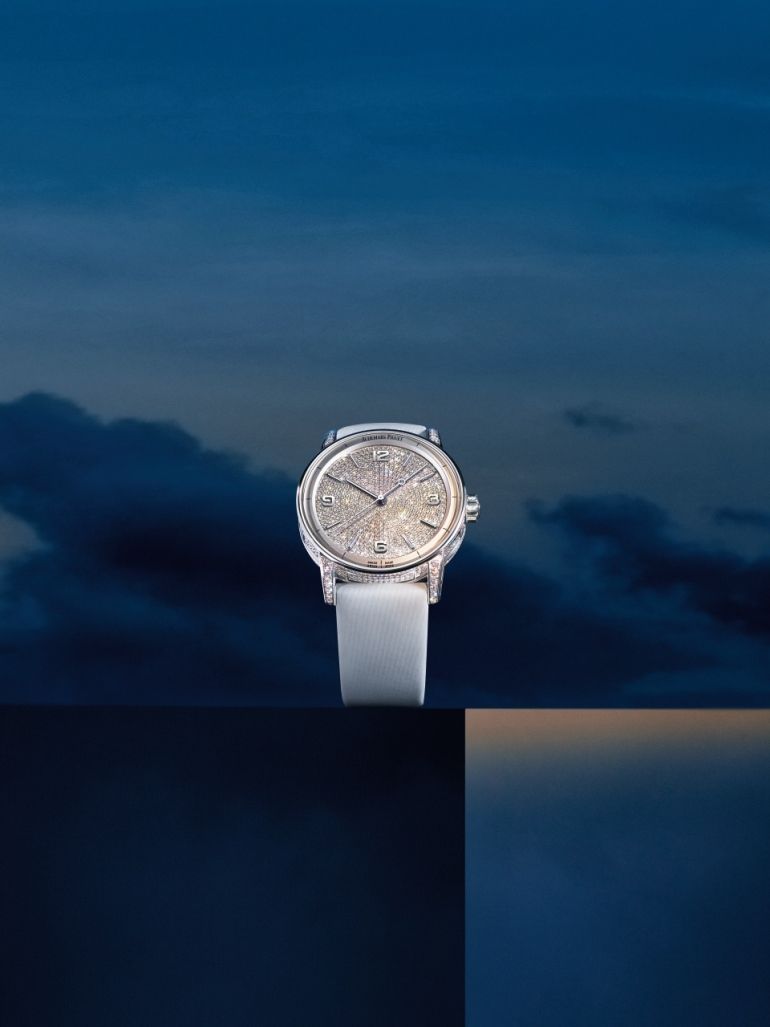 Elegant wristwatch with a diamond-encrusted bezel and white strap, set against a dark blue gradient background with cloud-like textures.