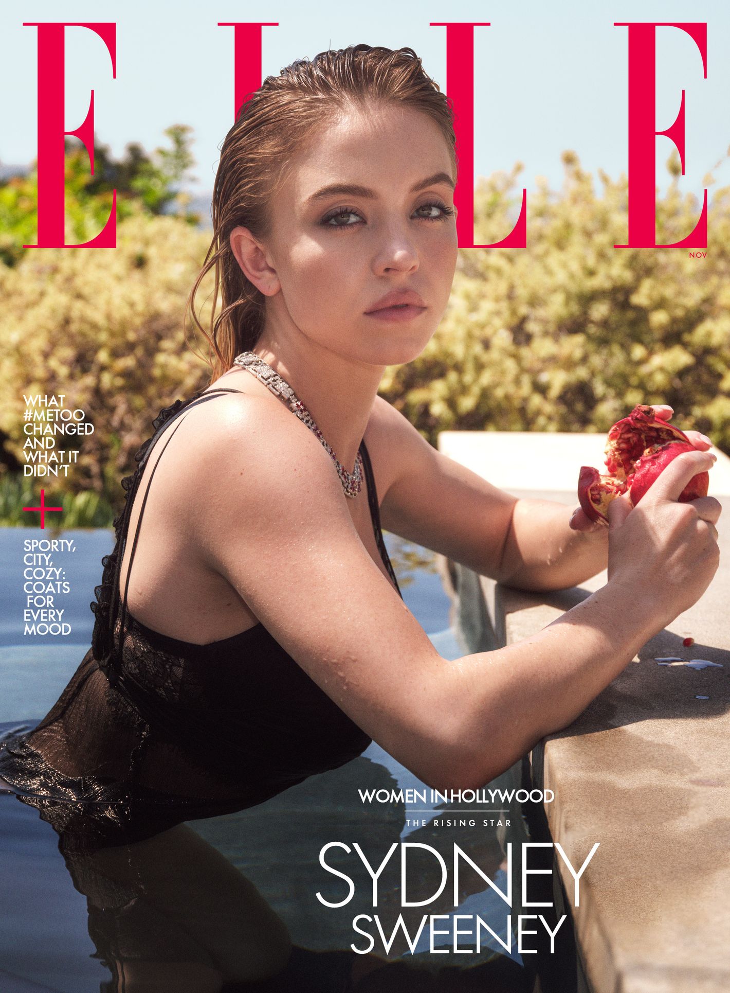 Sydney Sweeney is photographed for the cover of Elle magazine wearing a black sheer top in water, holding a pomegranate.