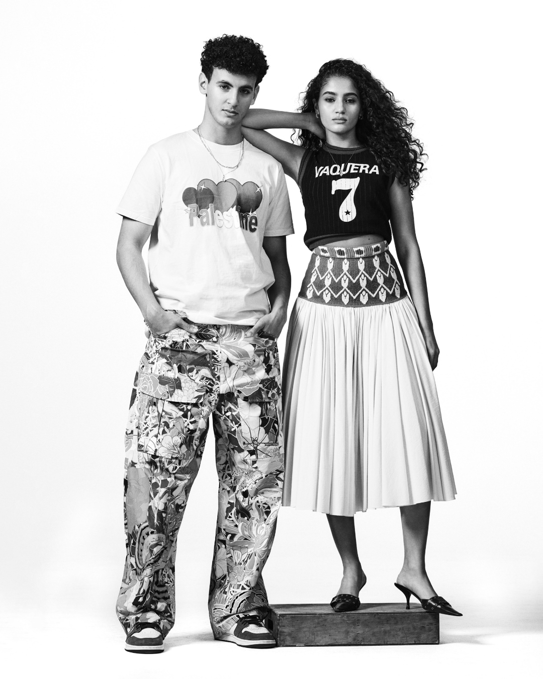 Monochrome studio shot of a male model with curly hair and a female model with long curly hair posing in fashionable streetwear.