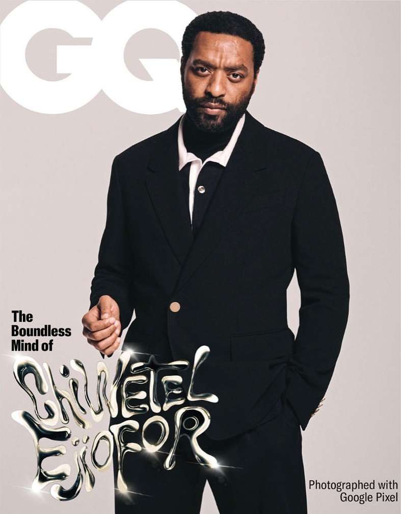 GQ cover featuring a Black man in a black suit with silver text overlay. The man has a beard and is centered in the frame.
