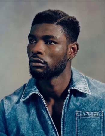 Portrait of a stylish Black man with short textured hair, wearing a denim shirt in a studio setting. Head and shoulders.
