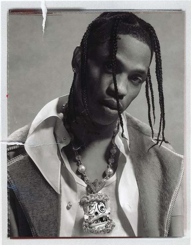 Portrait of a Black male with braided hair wearing a white shirt and a large pendant necklace against a light gray backdrop.