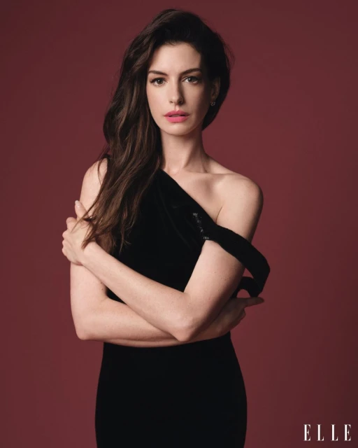 Portrait of Anne Hathaway wearing a black dress, posing with her arms crossed against a red background in a studio photoshoot.