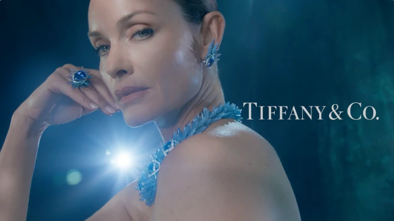 Close-up portrait of a woman wearing blue crystal jewelry including a statement necklace, matching earrings, and a large ring by Tiffany and Co.