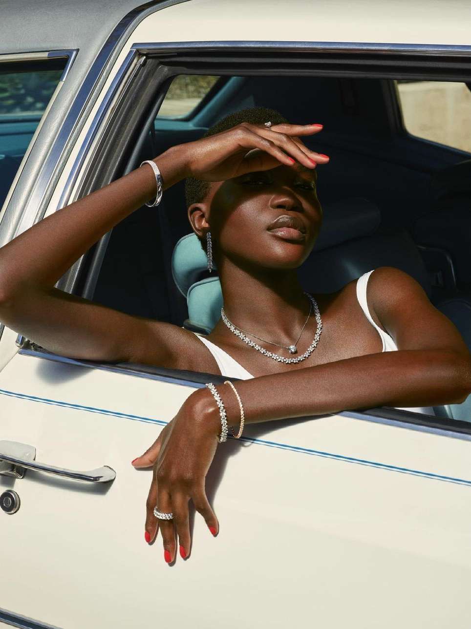 Elegant African woman poses in a classic car showcasing fine jewelry: diamond necklace, bracelet, and rings. Beauty shot, soft lighting.
