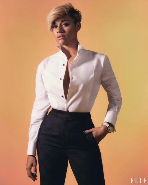 Stylish portrait of a woman in a white button-down shirt and black slacks against a yellow-to-orange gradient backdrop with a magazine logo.