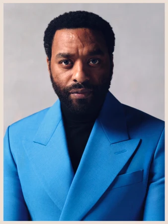 Portrait of Chiwetel Ejiofor wearing a vibrant blue blazer over a black turtleneck against a neutral studio backdrop