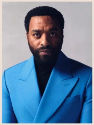 Portrait of Chiwetel Ejiofor wearing a vibrant blue blazer over a black turtleneck against a neutral studio backdrop
