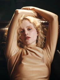 Portrait of a blonde woman wearing a fitted tan top with her arms raised behind her head by photographer Sharif Hamza