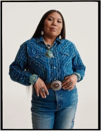Woman in blue patterned western shirt and jeans wearing ornate turquoise jewellery and a large silver pendant necklace against white