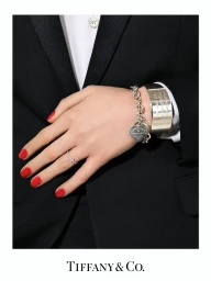 Close-up of a hand with red nail polish wearing silver bracelets and rings against a black suit, photographed by Sharif Hamza.