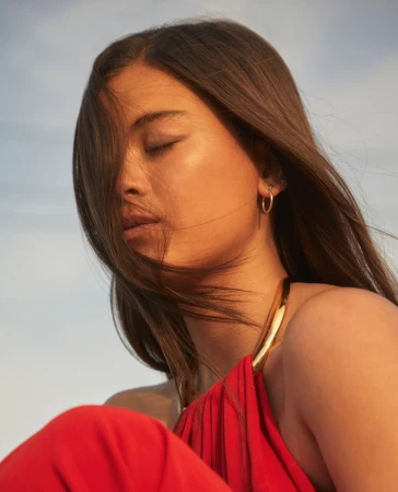 Close-up portrait of a woman with long brown hair wearing a red halter dress against a clear sky, photographed by Thomas Giddings.