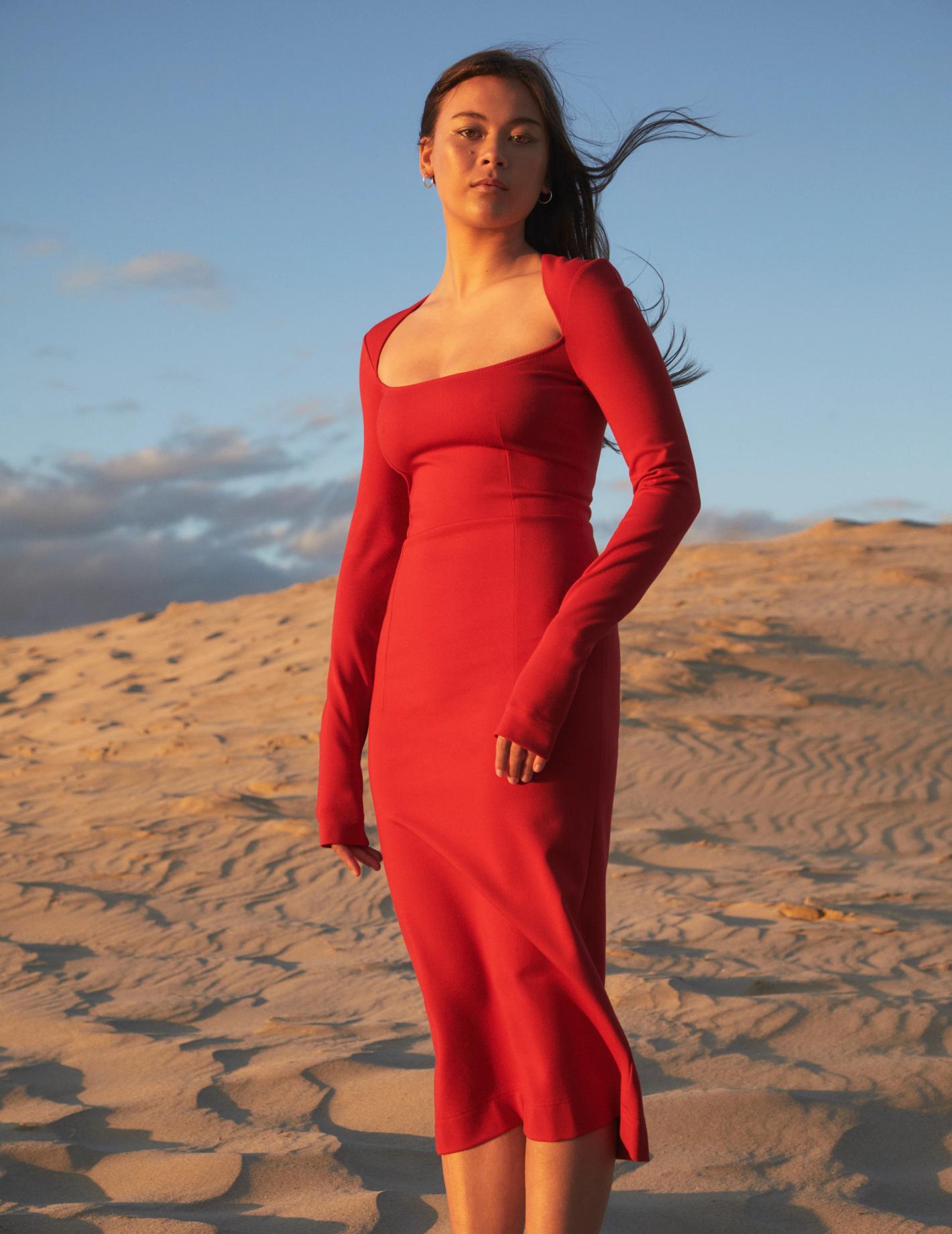 A woman in a long-sleeve red dress poses in the desert with a blue sky backdrop, bathed in the soft, warm light of the setting sun.