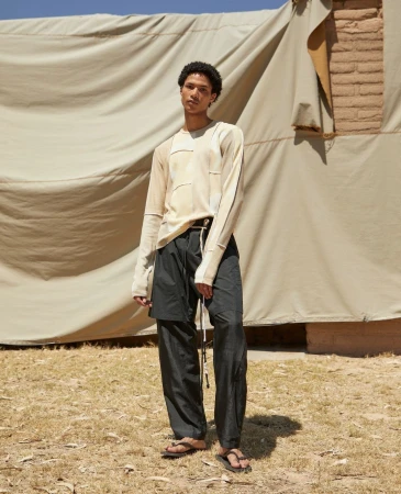 Young black man standing outdoors wearing a light long-sleeve patterned top and dark trousers by photographer Thomas Giddings.