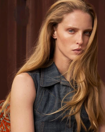 Portrait of a blonde woman wearing a dark denim vest against a warm textured background photographed by Thomas Giddings.
