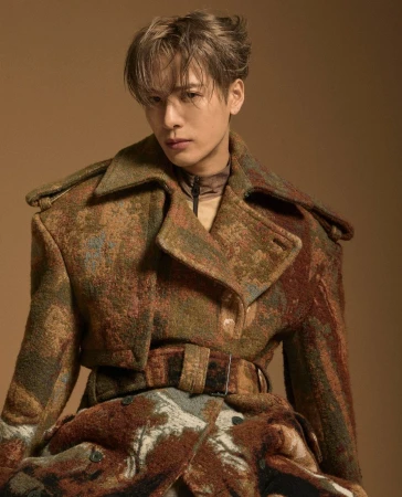 Adult male with light brown hair wearing a patterned brown jacket poses in a studio setting with neutral tan background. Fashion editorial.