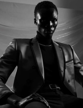 Striking black and white portrait of an African male model in a suit and turtleneck against a neutral backdrop with soft lighting.