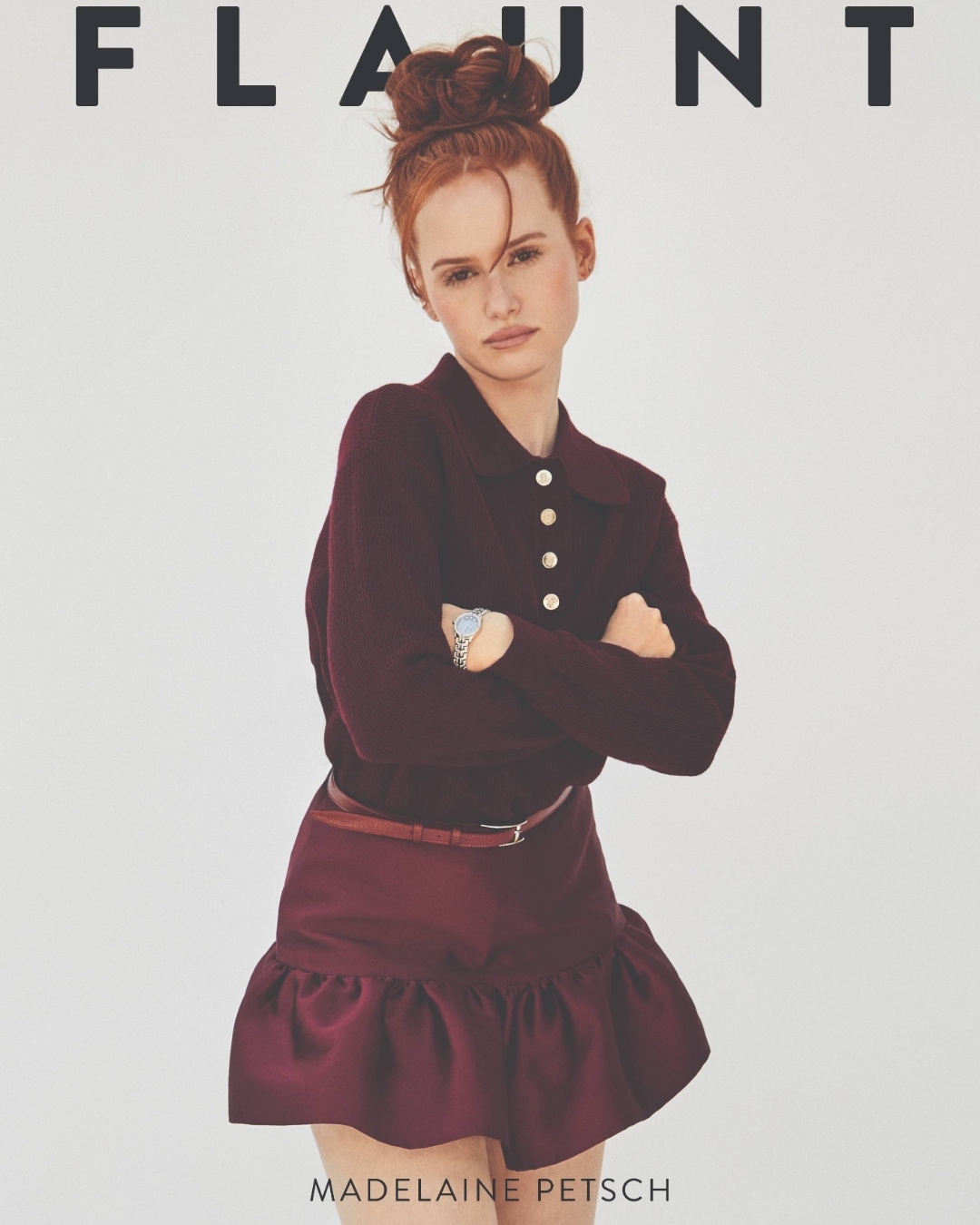 Madelaine Petsch poses on a magazine cover with a maroon sweater and skirt, standing against a white background with arms crossed.