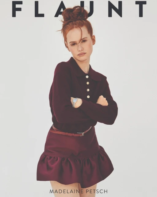 Madelaine Petsch poses on a magazine cover with a maroon sweater and skirt, standing against a white background with arms crossed.