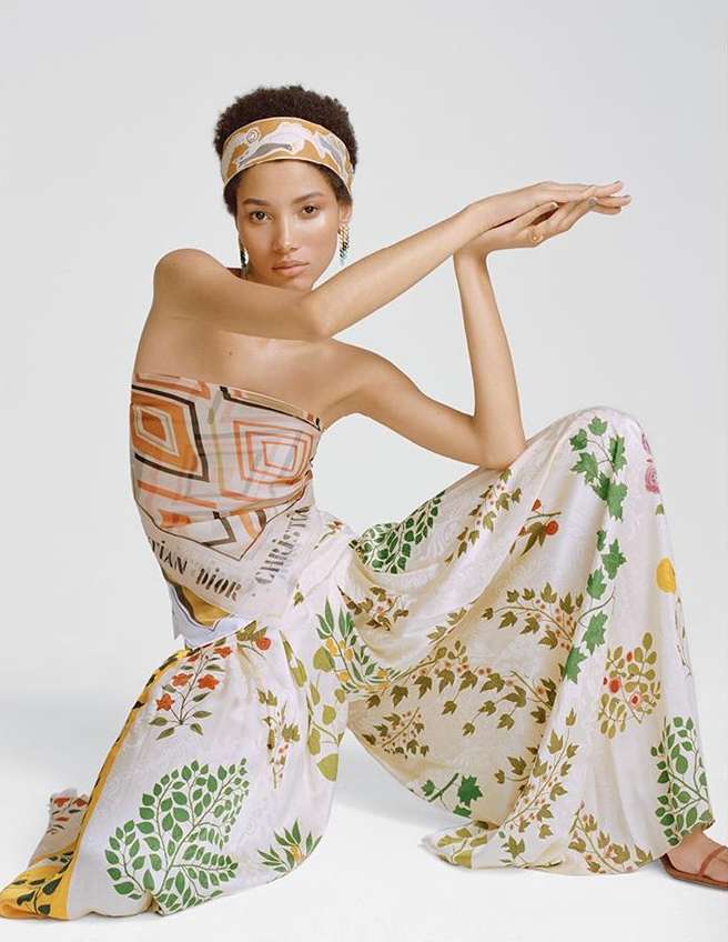 Elegant model in floral print wide-leg pants and headscarf poses in a studio, exuding high fashion and style against a plain white backdrop.