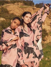 Two models wearing pink silk pyjamas with black panther prints posing outdoors against a dry hillside.