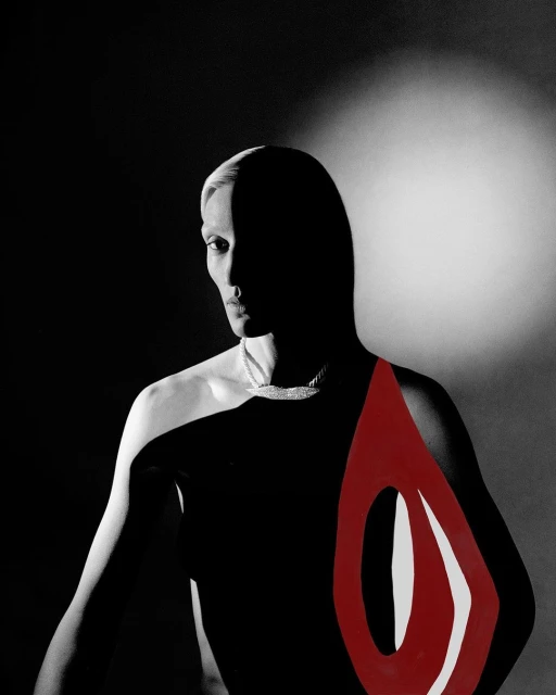 Striking black and white portrait of a person with platinum blonde hair, wearing a necklace, and accentuated with red paint on their chest.