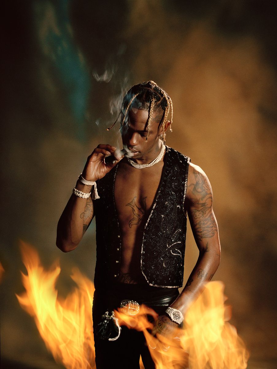 Adult male model posing in a sleeveless vest with jewelry, smoking with a flame effect in the foreground, in a medium shot.