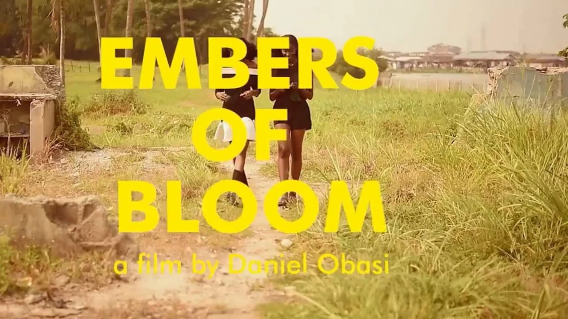 Two young women walk on a grassy path in a rural setting. Title text overlay: "Embers of Bloom," film by Daniel Obasi. 