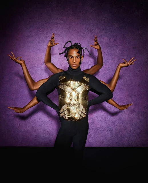 Person in black bodysuit poses with gold chest armor and multiple arms against a textured purple backdrop in a studio setting.