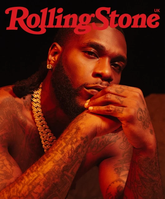 Close-up of Burna Boy on Rolling Stone UK cover, showcasing gold chain, bare chest, and arm tattoos against a dark background.