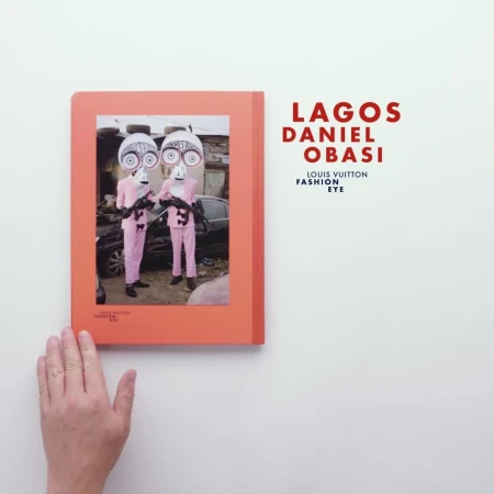 Book cover of "Lagos Daniel Obasi" shows two people in costume with masks and pink suits, standing outside, next to damaged vehicles.