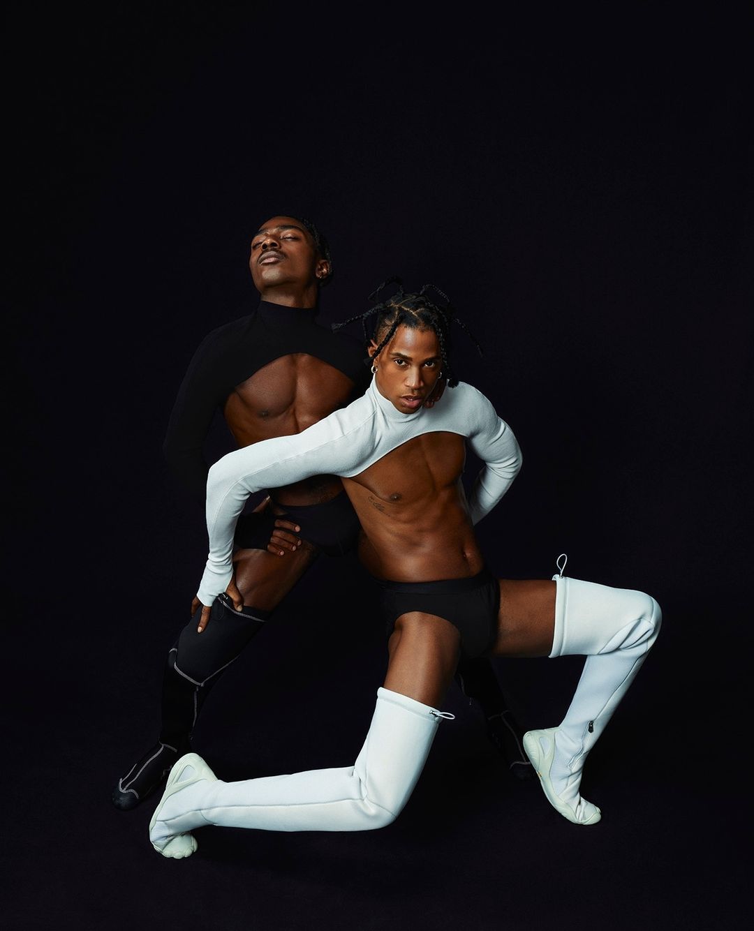 Two adult male dancers in partial bodysuits strike a pose against a dark background in a studio. Fashion and fitness concept.
