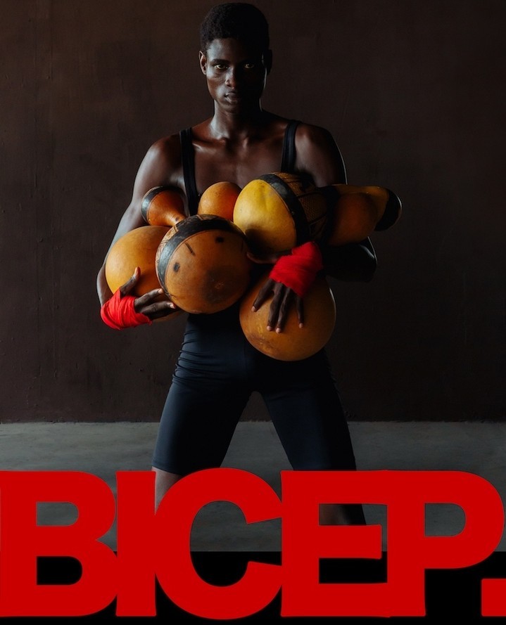 An athletic-looking Black man poses holding orange ball-shaped objects; red text 'BICEP' is in the foreground against a neutral background.