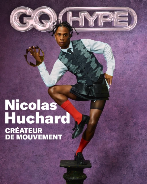 GQ Hype fashion editorial featuring a stylish Black male model in a vest and kilt, holding a crown, posing on a pedestal against a textured backdrop.