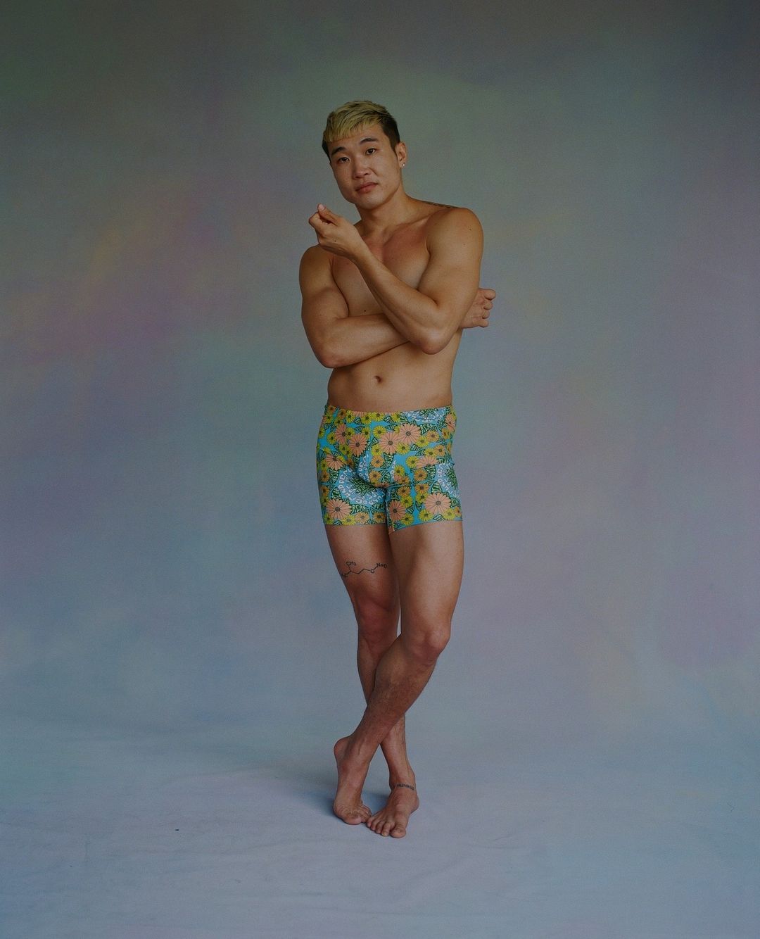 Athletic build Asian man with bleached hair poses in patterned yellow and blue boxer briefs in a studio, showcasing fashion and fitness.